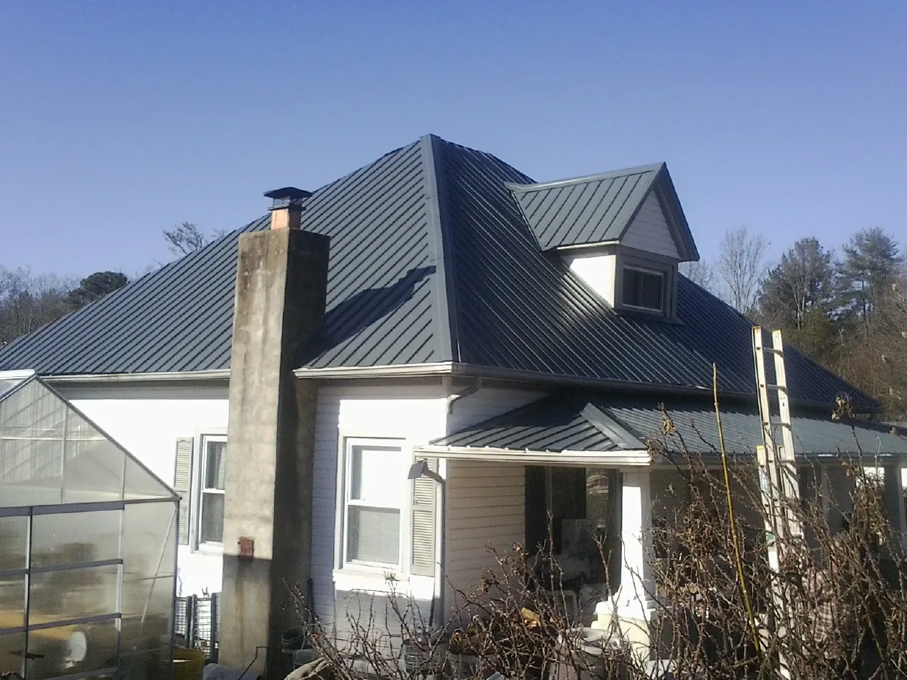 Dark blue standing seam metal roof on a white farmhouse with dormer — Slate & Tile Roof Repair by Roofing Brothers in Honeoye Falls