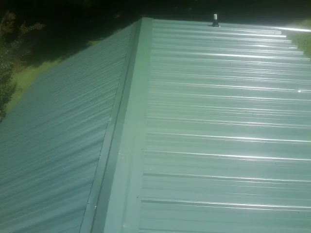 New green metal panels meeting at the ridge of a roof — Flat Roof Repair work by our crew in Honeoye Falls