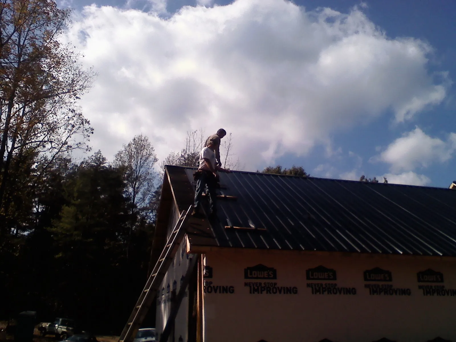 Roofer fastening dark metal panels high against a cloudy sky, from a Roof Inspection job in Honeoye Falls