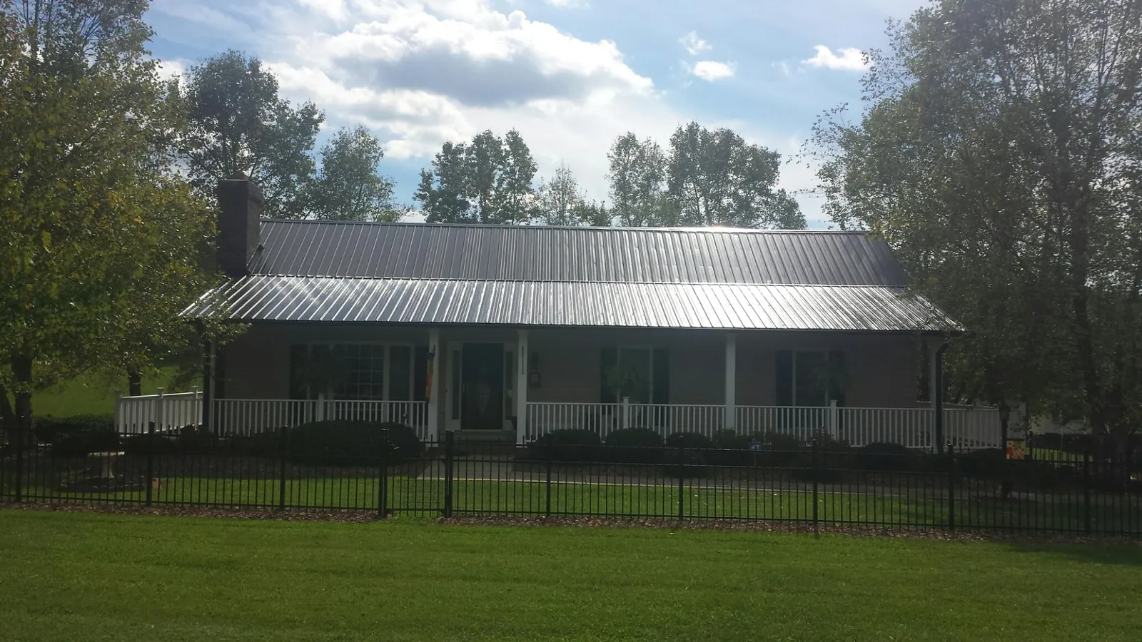 Gray metal roof on a brick ranch with a full width front porch — Gutter Guard Installation work by our crew in Honeoye Falls