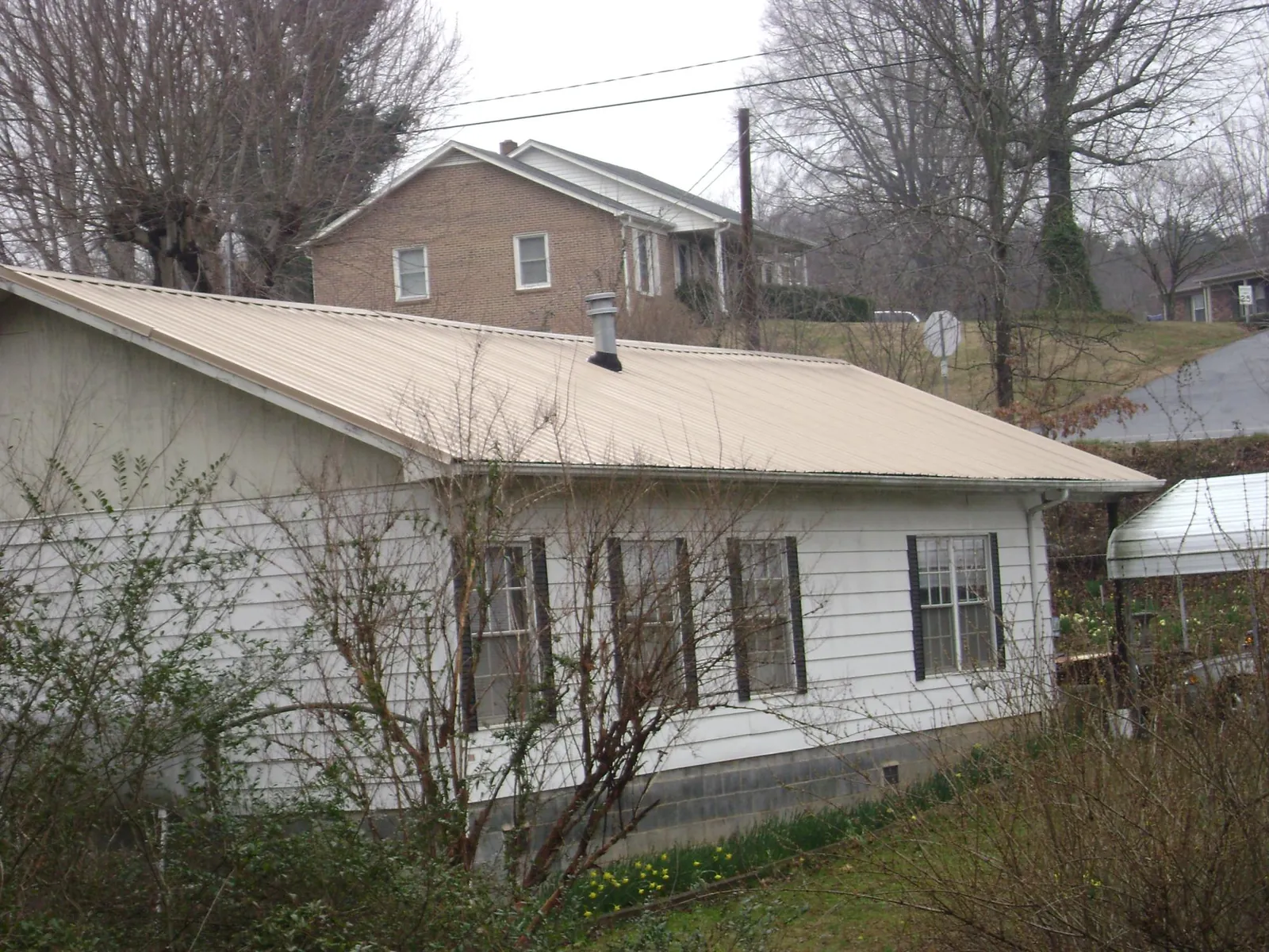 Tan metal roof on a white sided house set into a hillside — Commercial Roofing by Roofing Brothers in Honeoye Falls