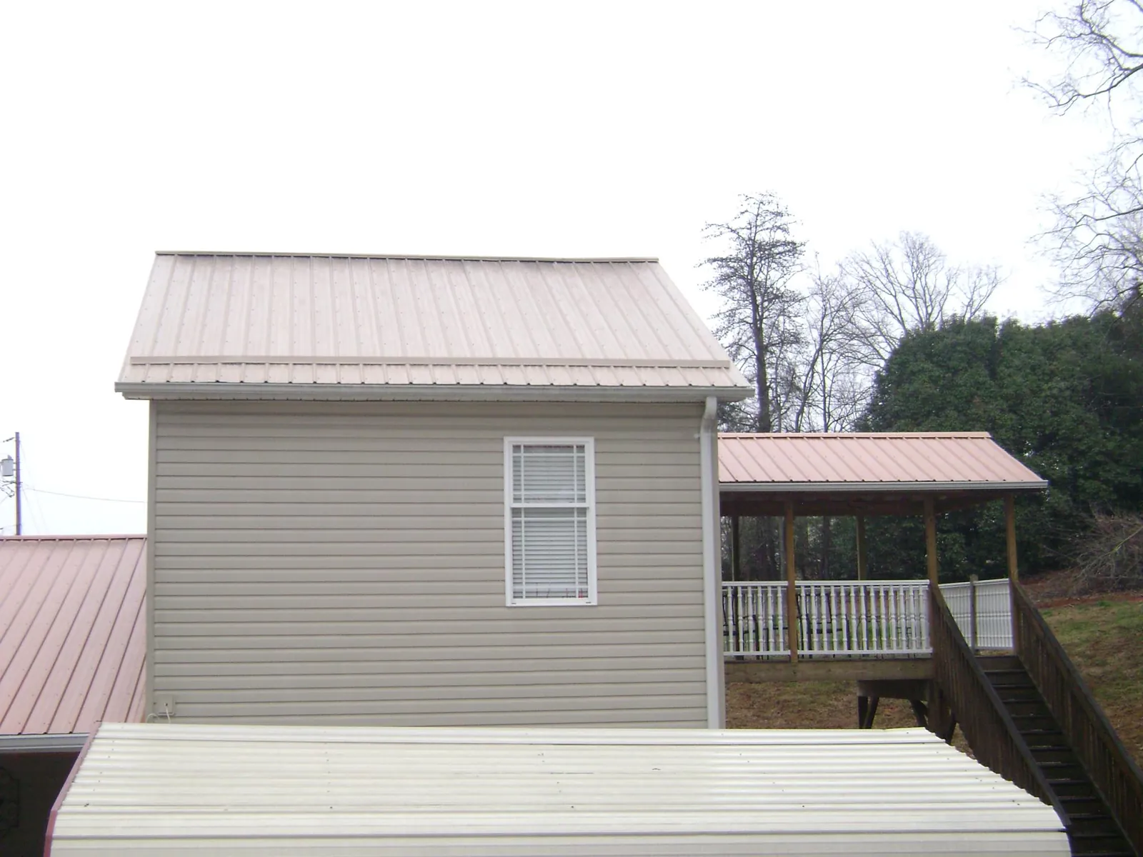 Tan metal roofs on a two story addition and attached porch, from a Roof Replacement job in Honeoye Falls
